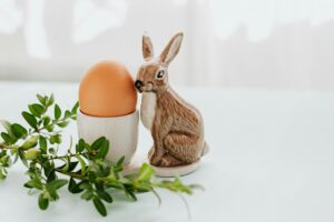 Osterei im Becher neben Keramik-Osterhase und grünen Zweigen – Symbolbild für Ostergeschenk und mögliche Schenkungsteuer bei Geldzuwendungen