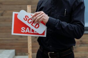erson bringt ein Sold-Schild an einem Verkaufsschild an – Symbolbild für Betriebsveräußerung nach Erbfall und steuerliche Folgen beim Unternehmensverkauf