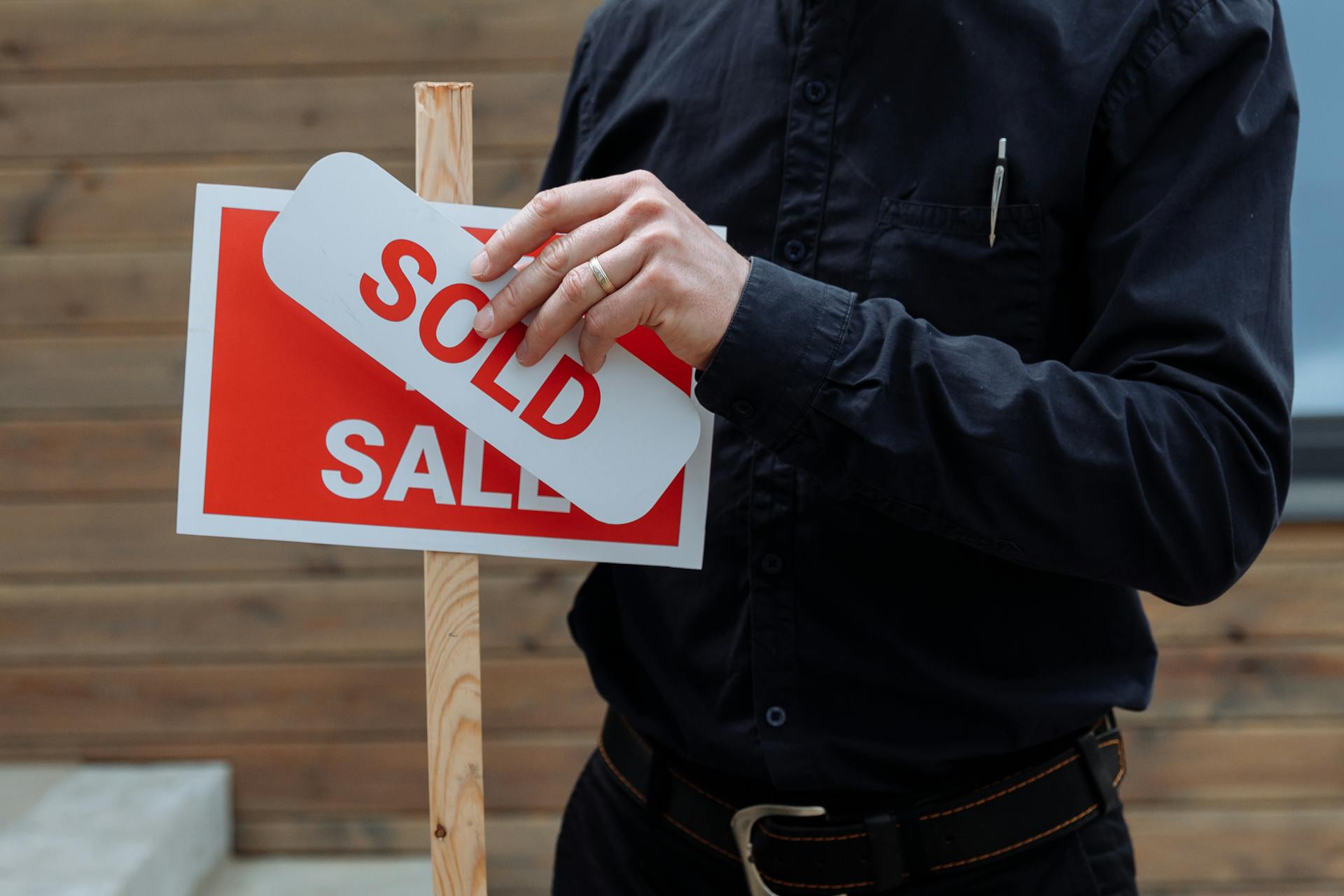 erson bringt ein Sold-Schild an einem Verkaufsschild an – Symbolbild für Betriebsveräußerung nach Erbfall und steuerliche Folgen beim Unternehmensverkauf